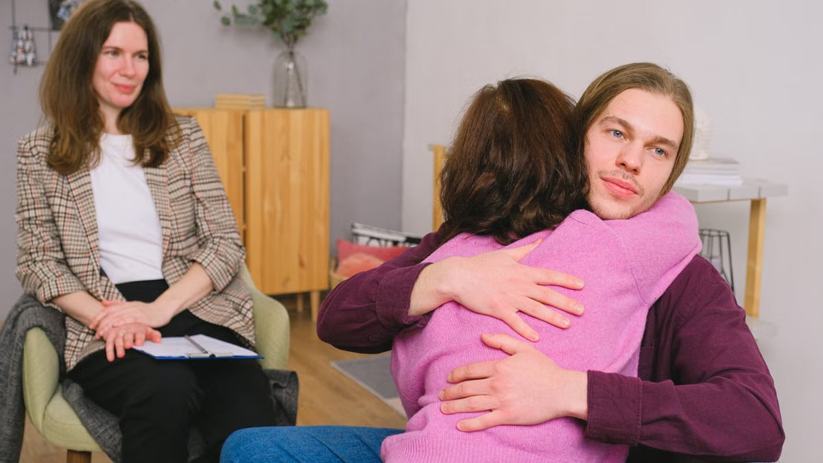 Calm couple in casual clothes sitting and embracing during session with psychologist in light room with wooden furniture